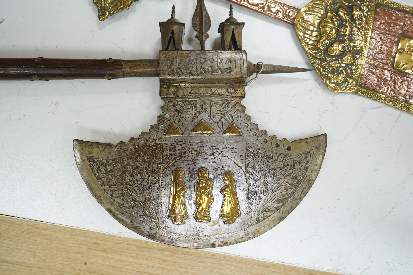 A decorative Indian axe, the large head inlaid with brass Hindu figures, together with a brass mounted North Indian kukri, another similar knife with bone handle, and a large shovel-shaped copper and brass item possibly
